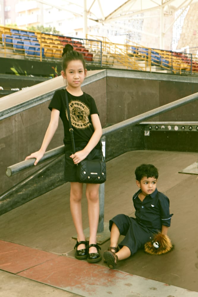 Gyzelle Tang (L): Bomber jacket, Armani Junior. Shirt, Young Versace. Leather skirt and Mary Janes, both model's own. Bag, Love Moschino. Leo Siva (R): Shirt, Armani Junior. Shorts, Paul Smith Junior. Charm, Fendi. Shoes, model's own.