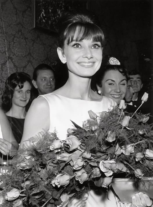 Image: Getty; The ever-graceful Audrey Hepburn with a bouquet of roses in 1965