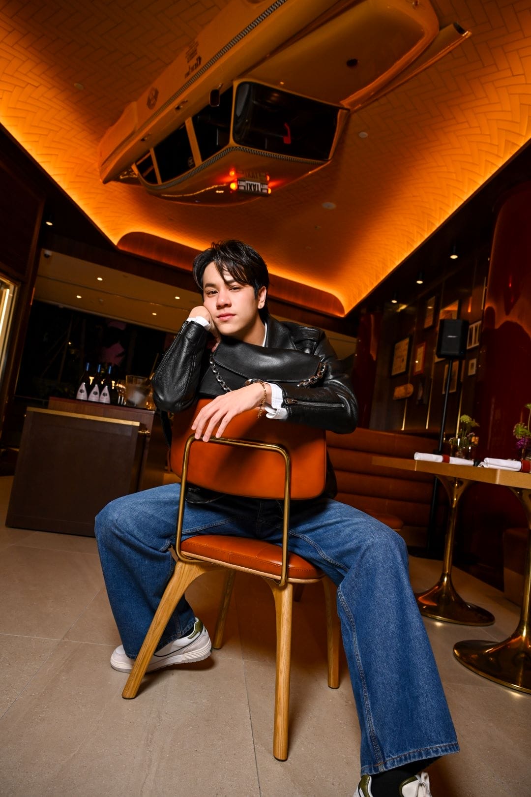 Thai actor Nanon is straddling a wooden chair at The Coach Restaurant in Jewel Changi Airport