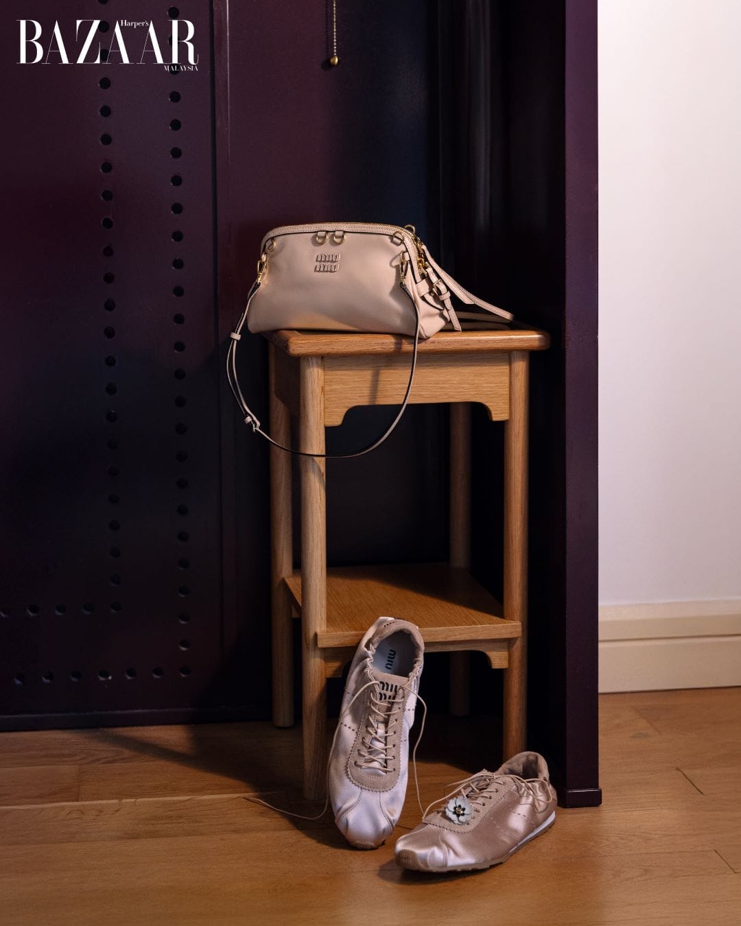 Light pink Miu Miu bag is on a night stand with ballet sneakers propped up against it