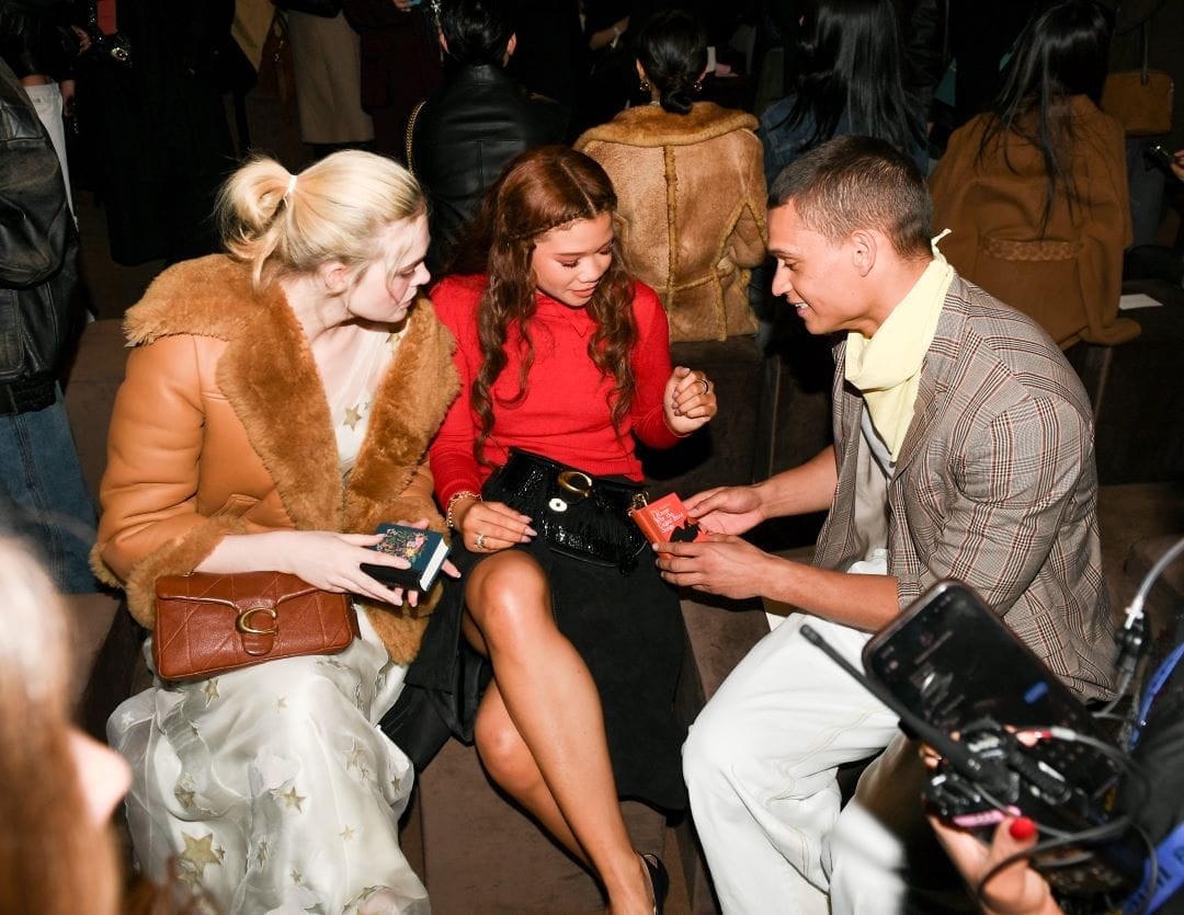 Elle Fanning, Storm Reid, and Tyriq Withers looking at Coach's mini book bag charms at the front row of Coach's Fall/Winter 2026 fashion show in New York. 