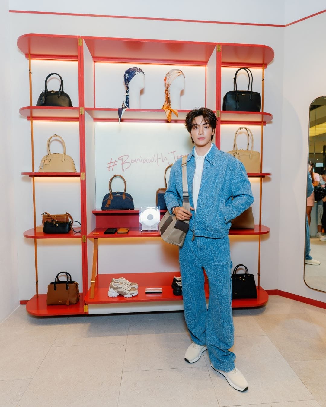 Thai actor Joong Archen poses in front of a shelf of Bonia bags